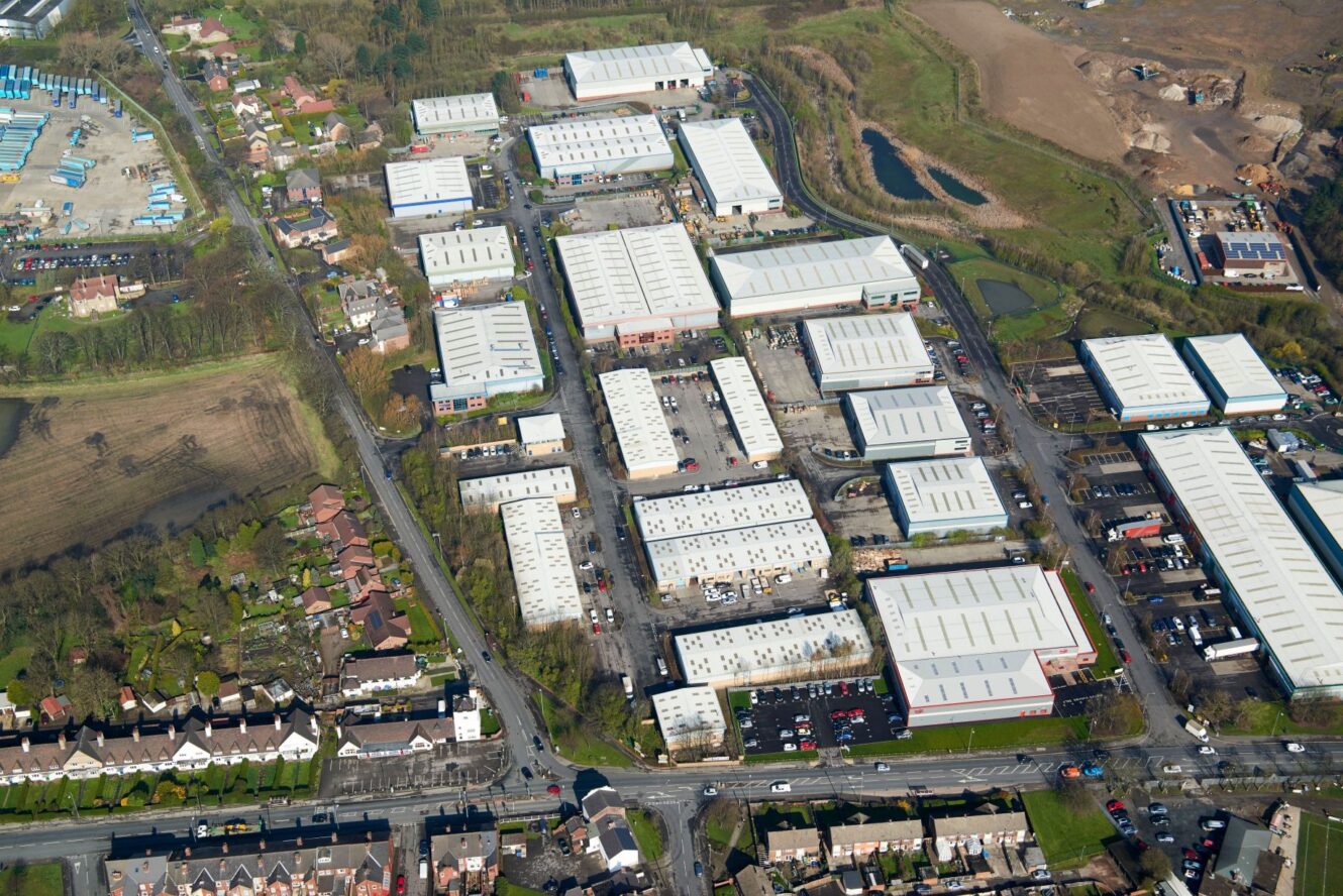 Aerial view of an industrial estate with multiple large warehouses, office buildings, parking lots, surrounding roads, and nearby residential areas.