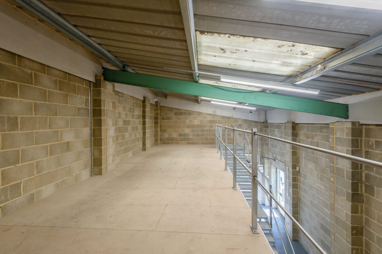 A mezzanine level in an industrial building with exposed brick walls, metal railings, and a corrugated metal ceiling.