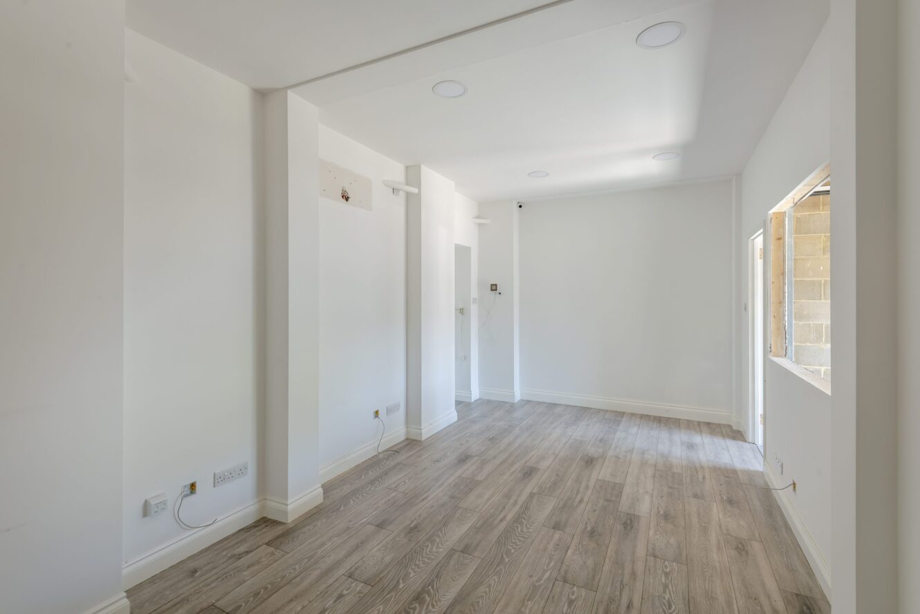 Empty room with white walls, light wood flooring, recessed ceiling lights, electrical outlets, and an unfinished window opening on the right wall.