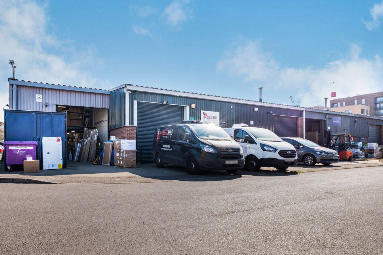 Several vans and vehicles are parked in front of a warehouse building with open garage doors. Boxes and pallets are stacked nearby on a clear day.