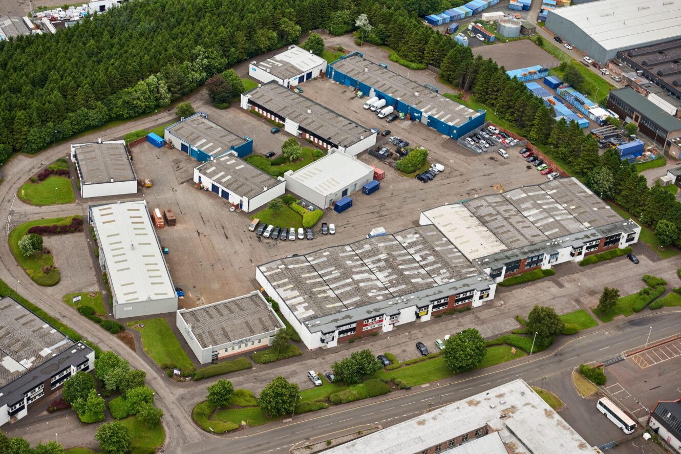 Aerial view of an industrial park with multiple warehouses, parking lots, and surrounding trees.