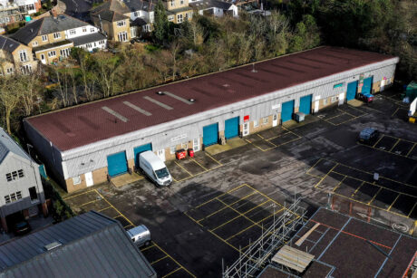 Aerial view of a long, single-story industrial building with multiple blue garage doors, a white van parked outside, and marked parking spaces in the lot.