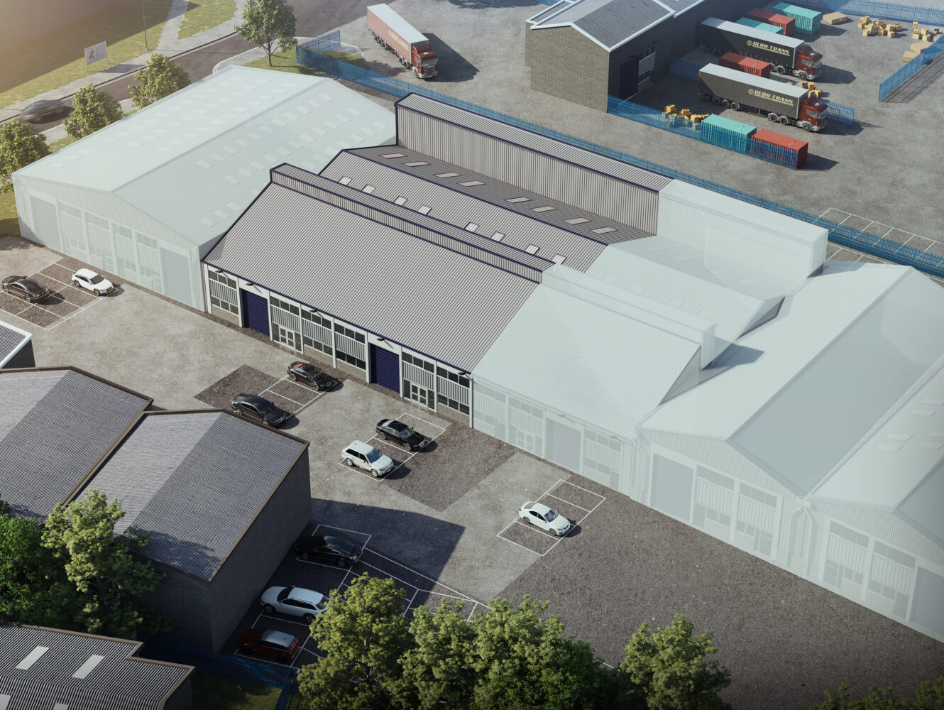 Aerial view of an industrial complex with multiple warehouse buildings, parked cars, and trucks in loading areas, surrounded by trees and paved roads.