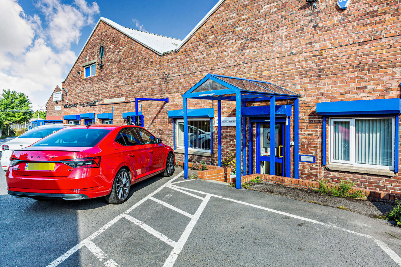 A red car is parked in a designated space outside a brick building with blue window and door frames.