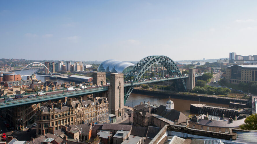 A view of Newcastle upon Tyne, showing the Tyne Bridge, surrounding buildings, and the River Tyne under a clear sky.