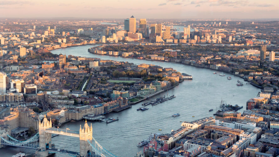 Aerial view of the River Thames winding through central London, with Tower Bridge in the foreground and modern skyscrapers in the background.