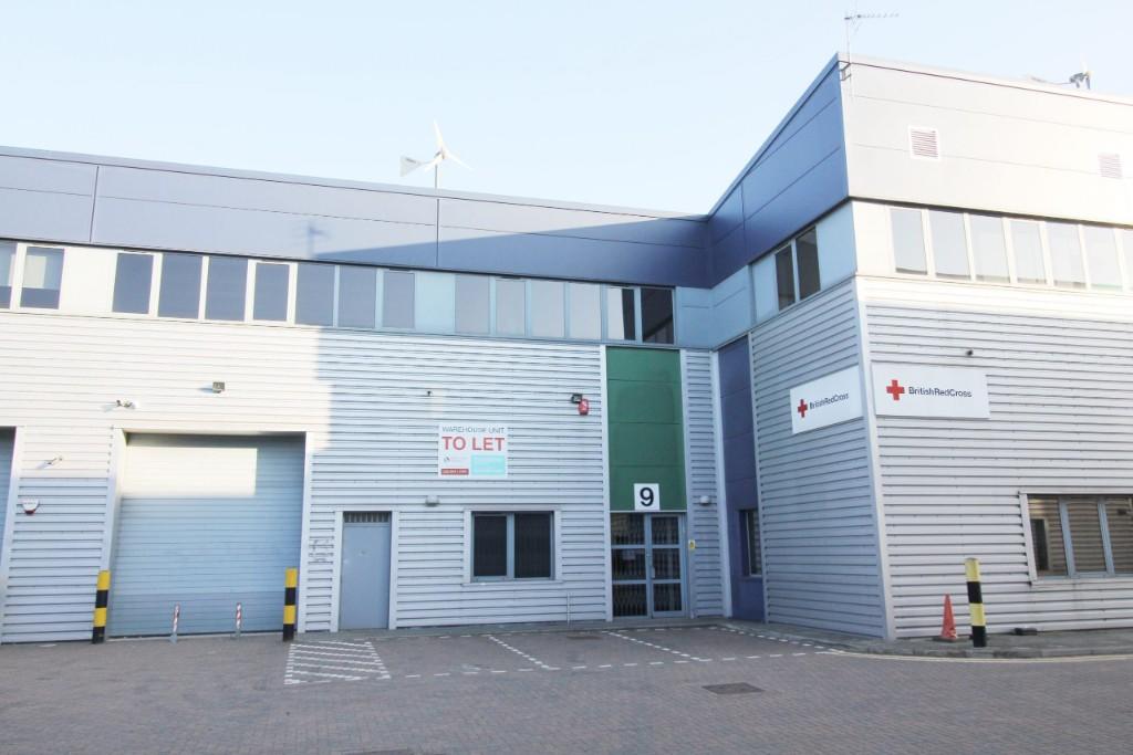 A modern industrial building with a sign reading TO LET and another for the British Red Cross, featuring a large garage door, entrance, and numbered door 9.