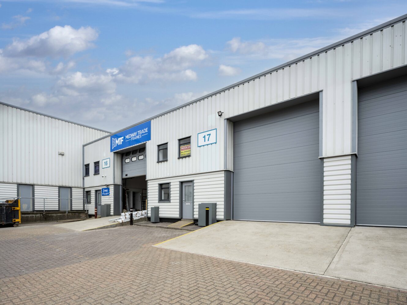 An industrial warehouse building with several large roller doors, a small entrance door, and a sign labeled JMF Motor Trade Centre.