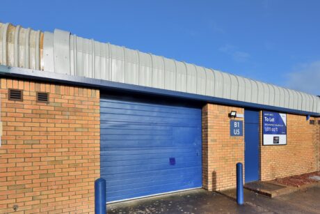 Single-story brick building with a blue garage door and a sign indicating toilets to the right. The roof is curved and metallic.