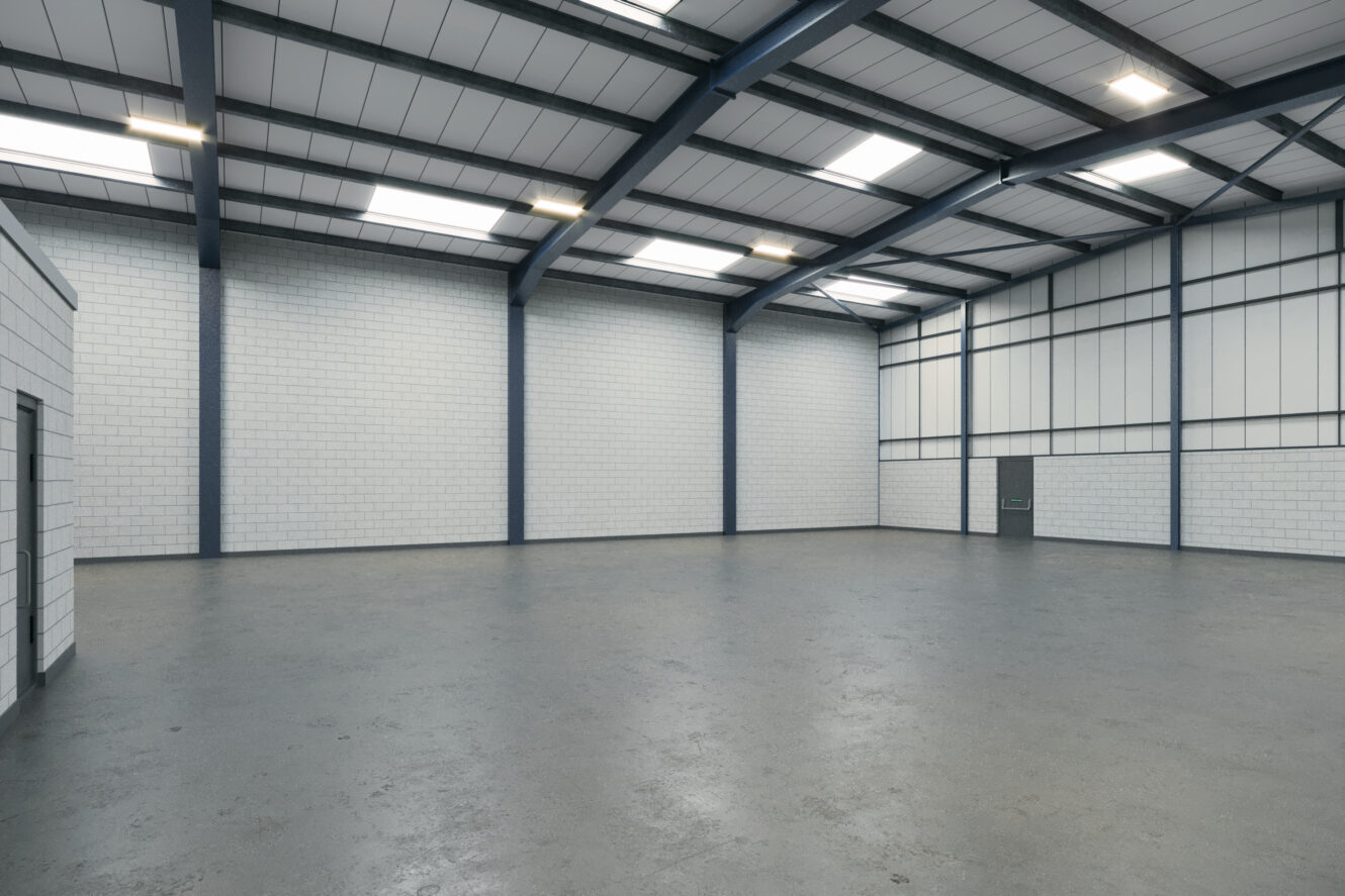 An empty industrial warehouse with concrete floors, white brick walls, metal beams, and skylights in the ceiling.