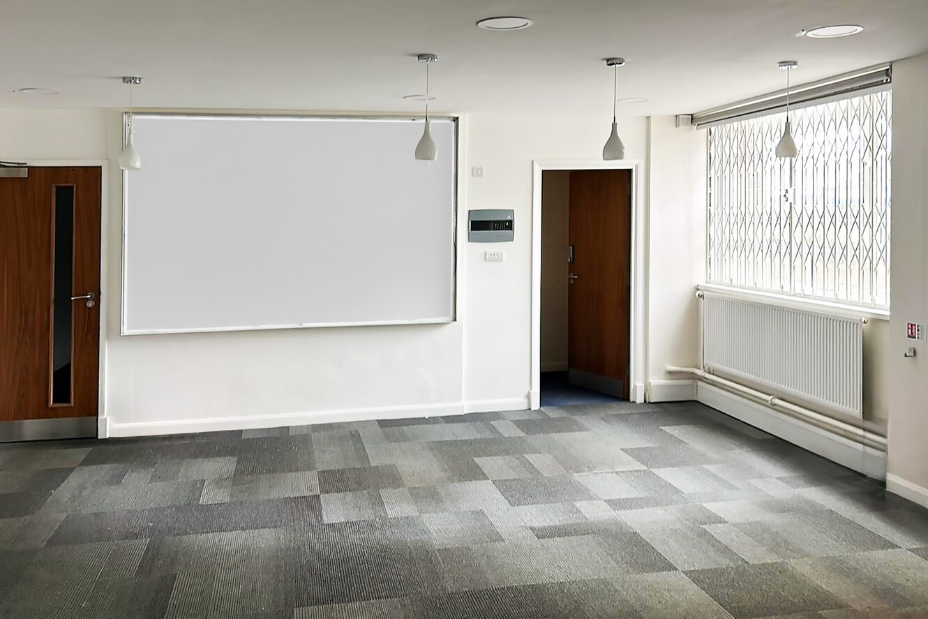 Empty room with gray carpet, white walls, a blank whiteboard, ceiling lights, large window with security bars, and two closed wooden doors.