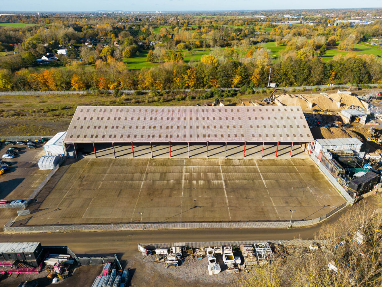 Aerial view of an empty industrial warehouse with an open yard, surrounded by trees and industrial materials, under a clear sky.
