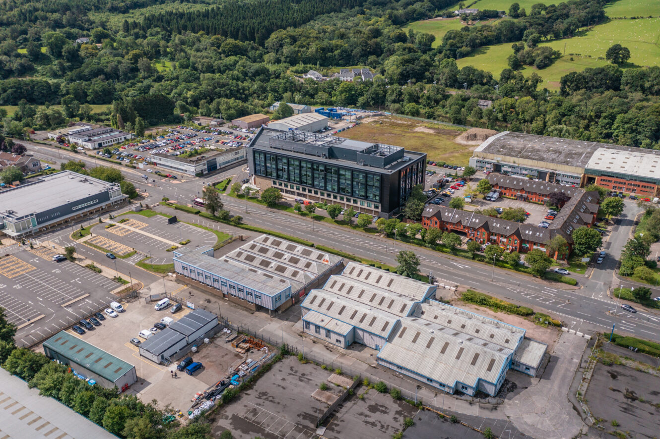 Aerial view of a business park with office buildings, warehouses, parking lots, and surrounding greenery.