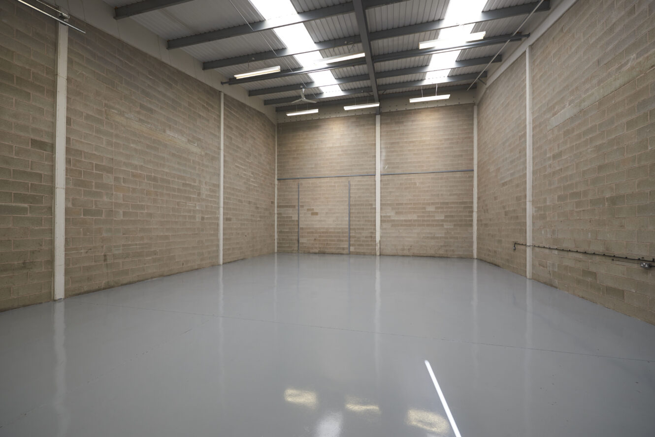 Empty industrial warehouse unit with bare brick walls, a polished grey concrete floor, and a metal roof with skylights allowing natural light inside.