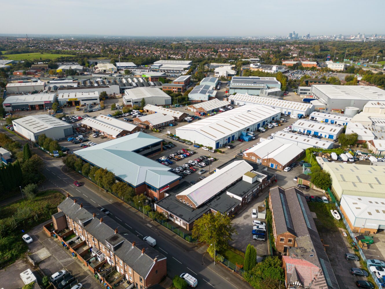 Aerial view of an industrial estate with warehouses, parking lots, and nearby residential houses on a clear day.
