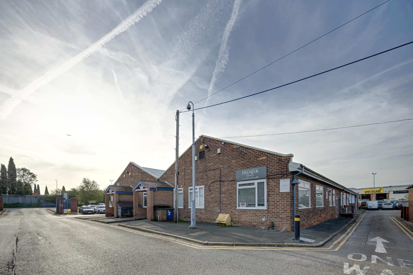 A single-story brick building on a quiet street with a sign reading Pharmar, under a sky with contrails and distant trees in the background.