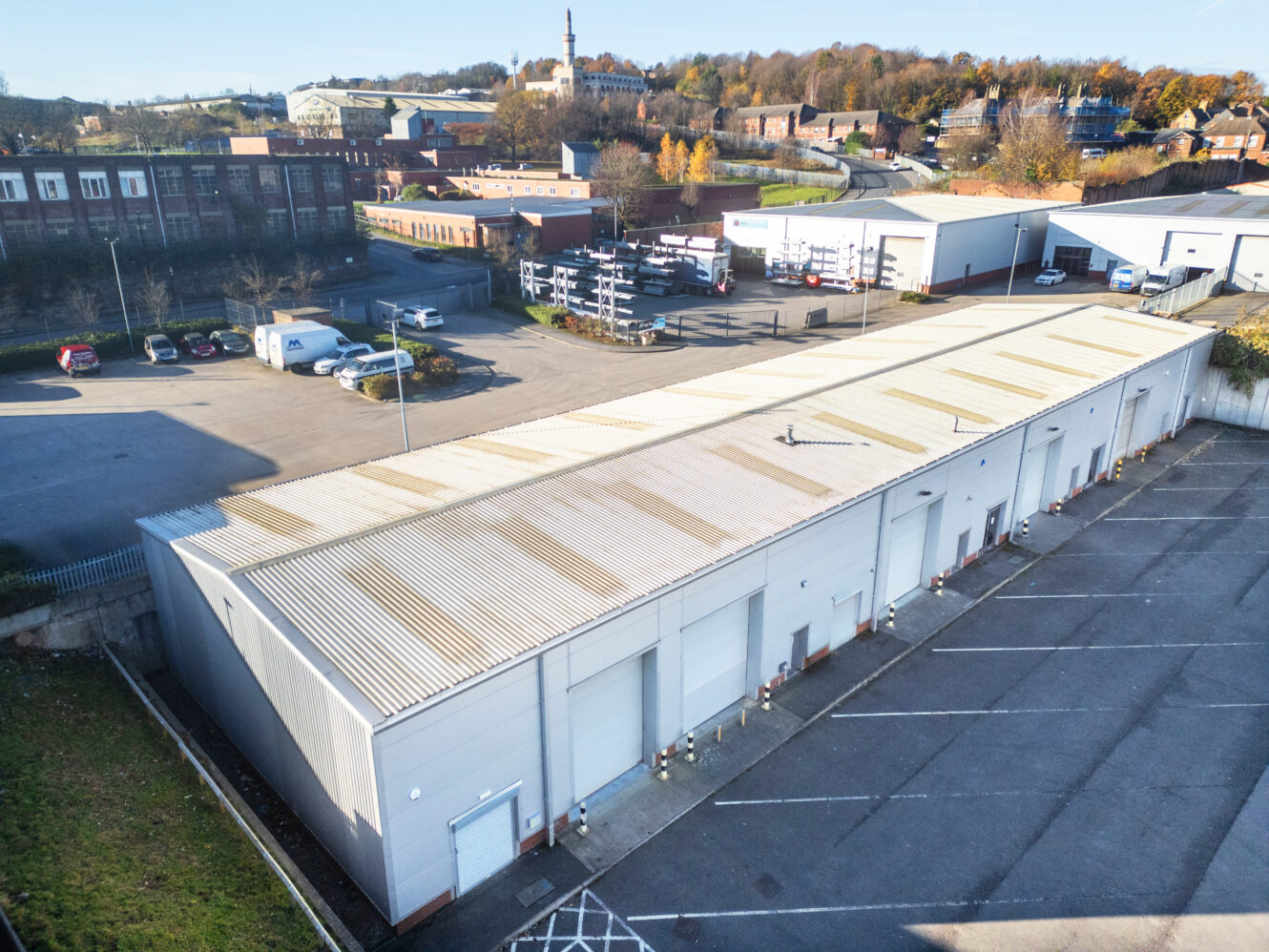 A large industrial warehouse with multiple loading bays and an adjacent parking lot, situated in an industrial area with buildings and trees in the background.