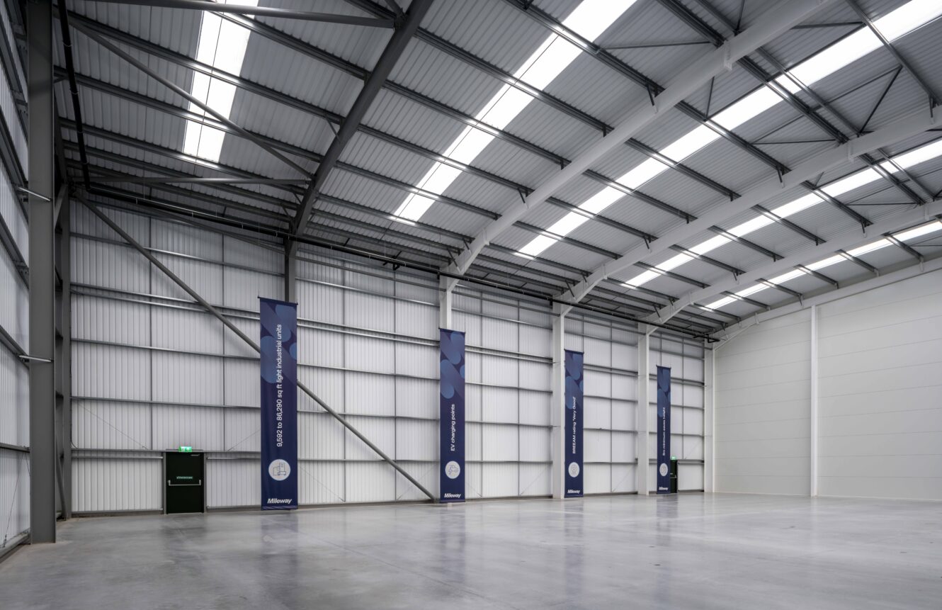 Spacious, empty warehouse interior with high ceilings, white walls, large windows, and vertical banners on the left wall.
