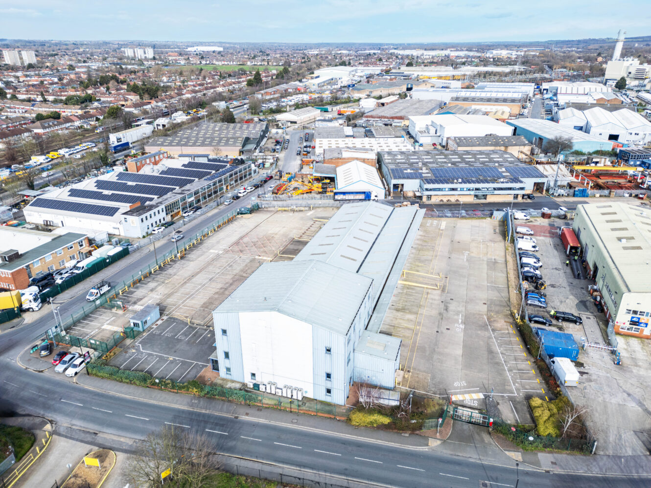 Aerial view of industrial warehouses, parking lots, and roads in an urban area with residential neighborhoods in the background.