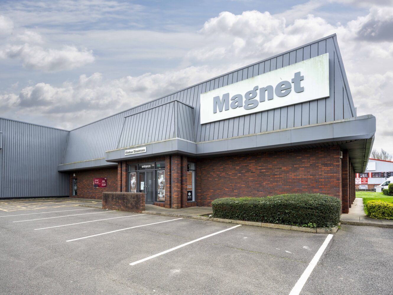 A commercial building with a large Magnet sign above the entrance, surrounded by an empty parking lot under a cloudy sky.