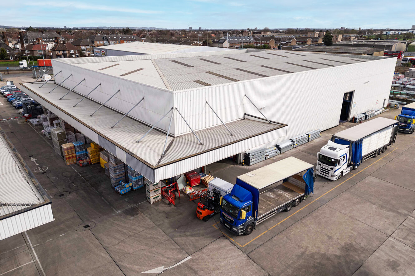 Aerial view of a warehouse with delivery trucks parked at loading bays and a forklift moving pallets near the entrance.