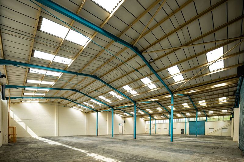 Empty warehouse interior with high ceiling, skylights, blue steel beams, white walls, and concrete floor.