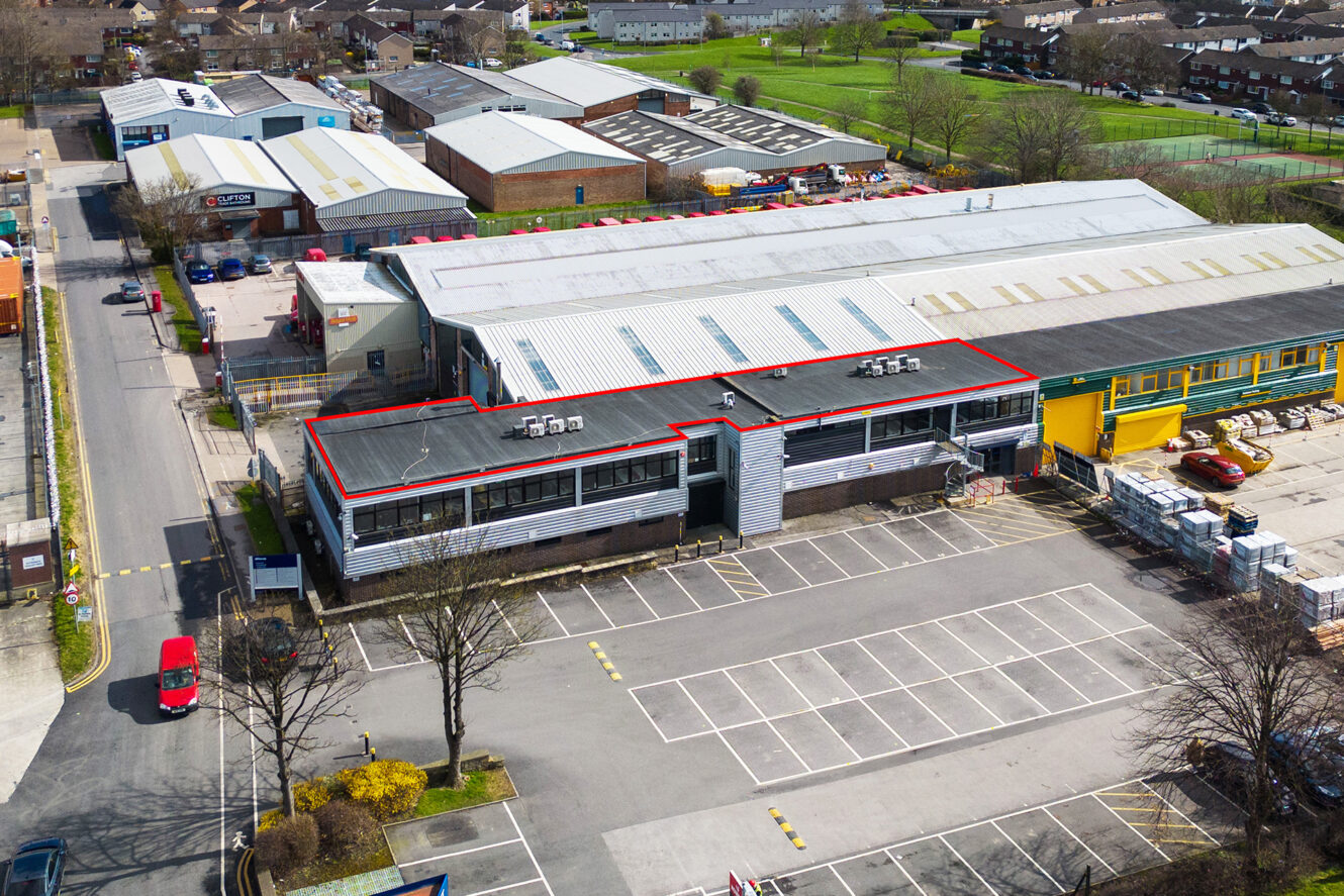 Aerial view of an industrial building with a red outline on the roof, surrounded by parking spaces and other commercial structures.