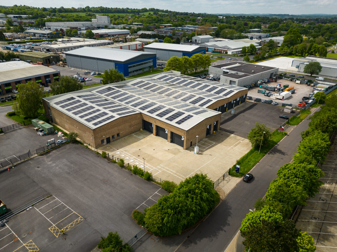 A large industrial building with solar panels on the roof, surrounded by parking lots, trees, and other commercial buildings.
