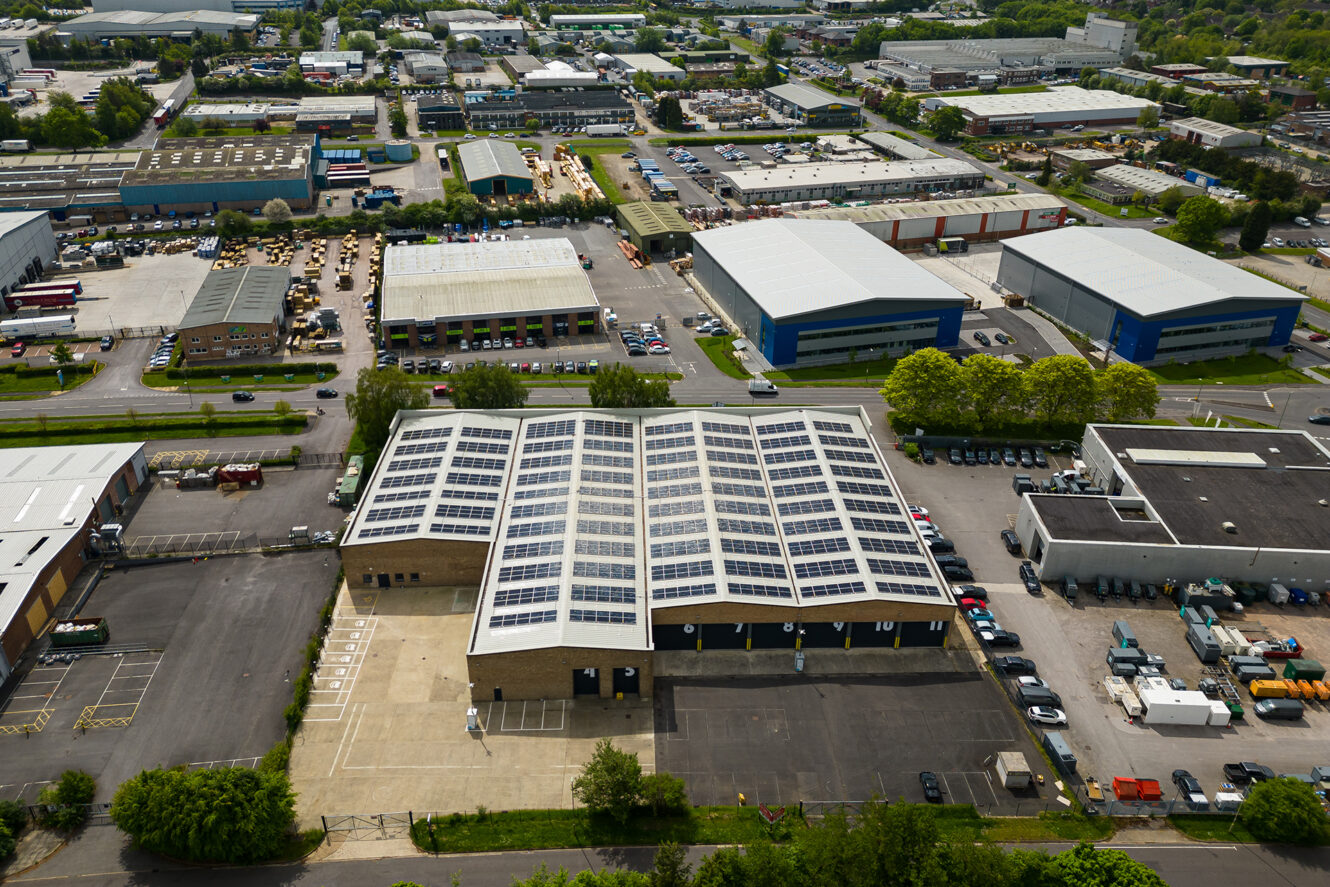 Aerial view of an industrial area with several warehouses, one of which has solar panels installed on its roof.