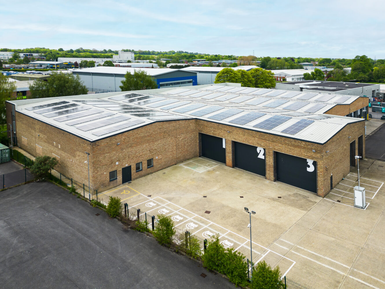 A large industrial building with solar panels on the roof, multiple garage doors numbered 1 to 3, and parking spaces in front.