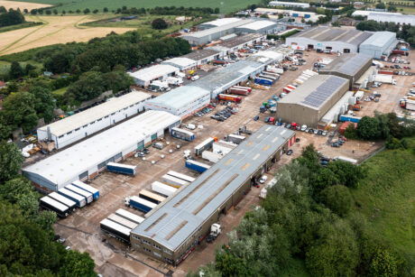 Aerial view of an industrial estate with multiple warehouses, parked trucks, trailers, and surrounding greenery.