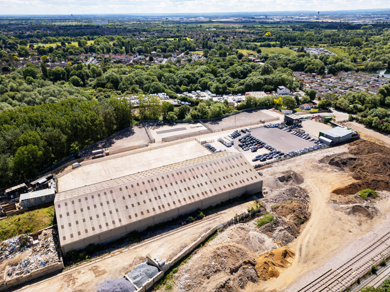 Aerial view of an industrial warehouse with adjacent parking lot, surrounded by trees, residential areas, and construction sites.