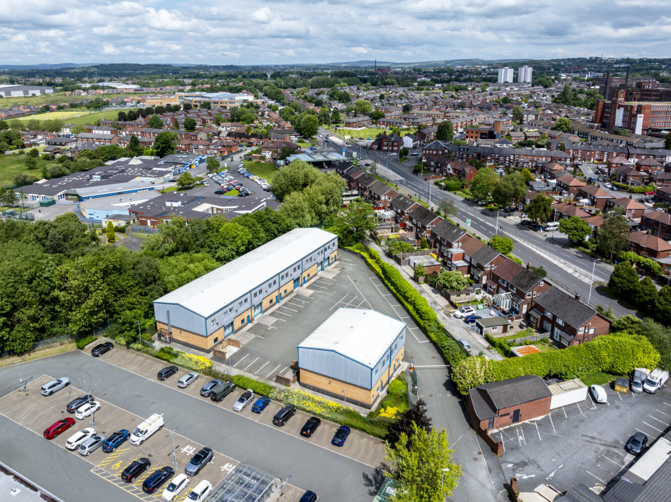 Aerial view of a suburban area with residential houses, commercial buildings, parking lots, and green spaces under a partly cloudy sky.