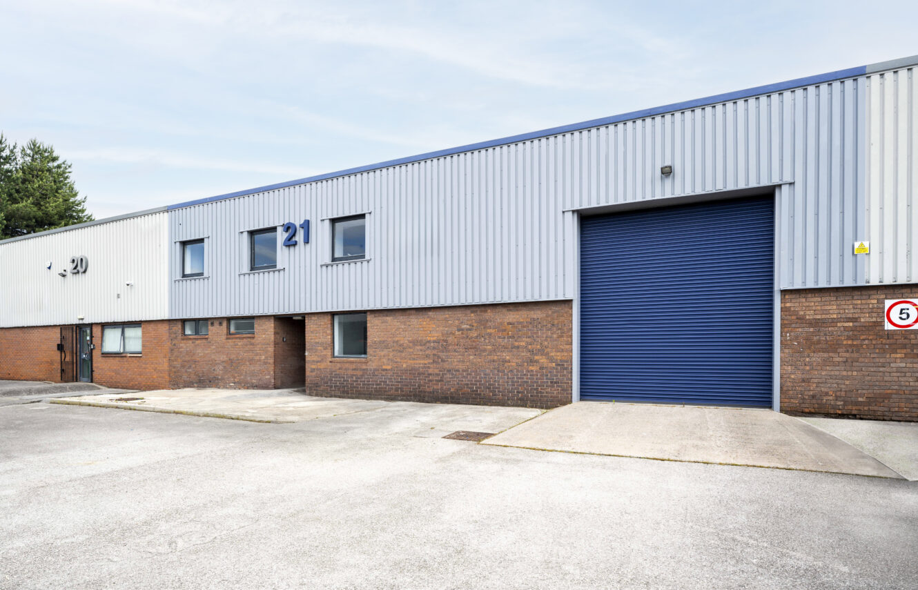 Industrial warehouse building with brick and metal exterior, blue roller shutter door, and number 21 displayed on the structure.