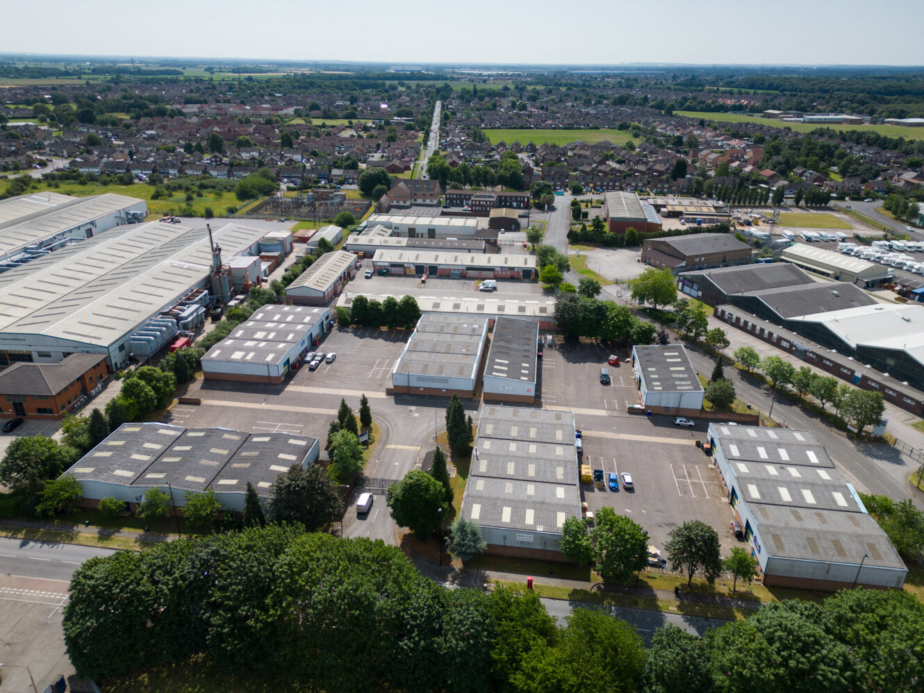 Aerial view of an industrial estate with multiple warehouse buildings, parking lots, and surrounding residential areas under a clear sky.