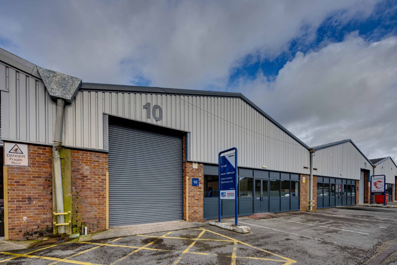Industrial warehouse building with brick and metal exterior, labeled 10, featuring a large closed roller door and adjacent parking spaces under a cloudy sky.