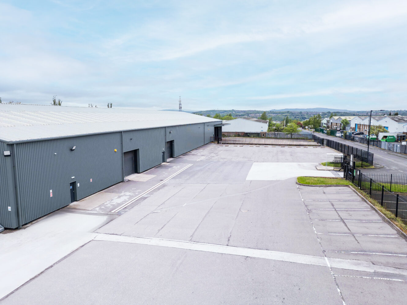 Large industrial warehouse with gray metal walls and multiple loading bay doors, adjacent to an empty paved lot under a clear sky.