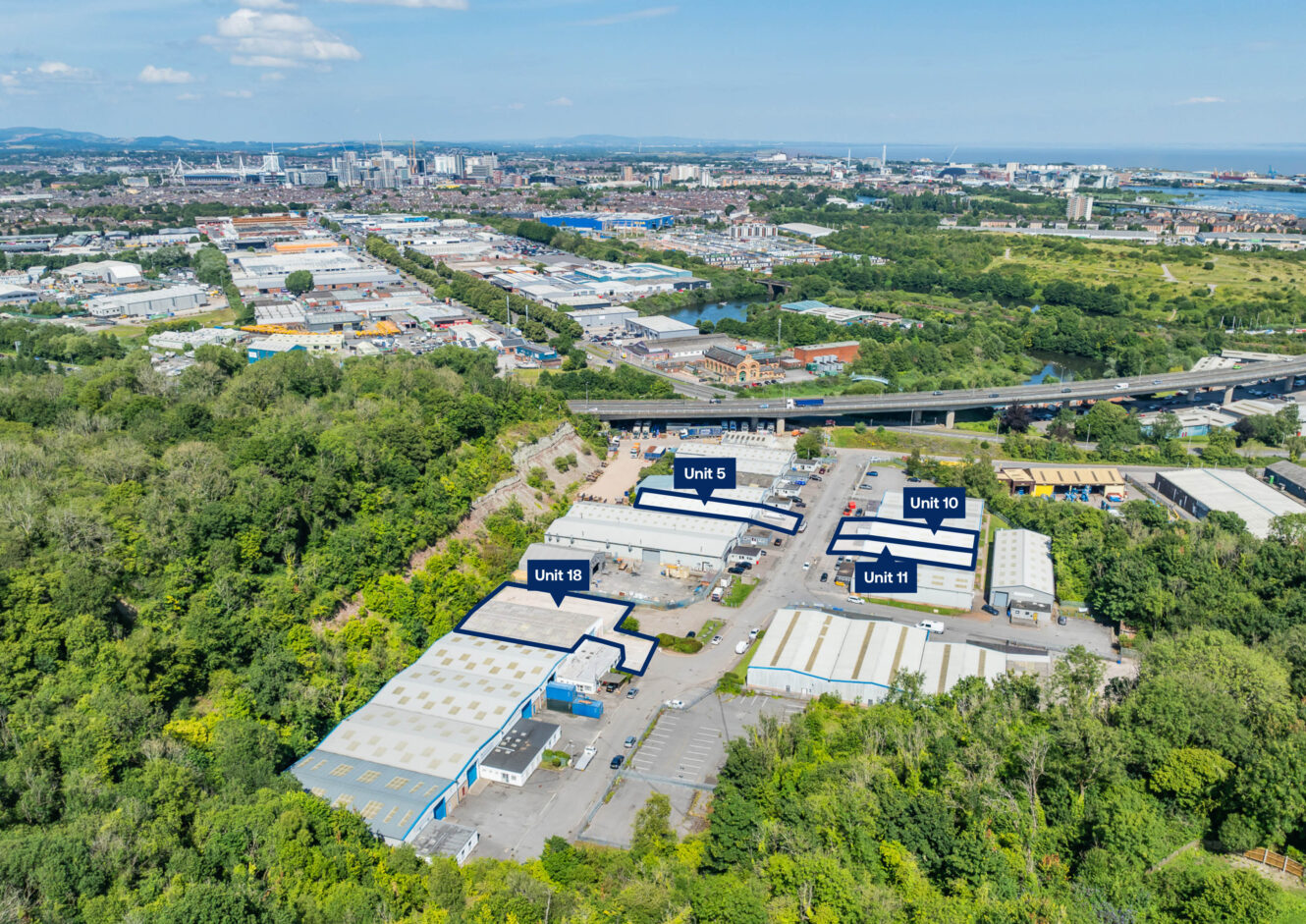 Aerial view of an industrial estate with Units 5, 10, 11, and 18 labeled, surrounded by trees and adjacent to a highway, with a cityscape in the background.