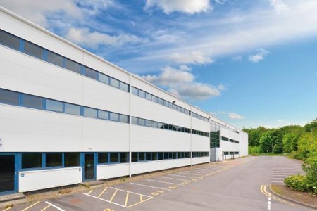 A large, modern white office building with tinted windows and an empty parking lot under a blue sky with scattered clouds.