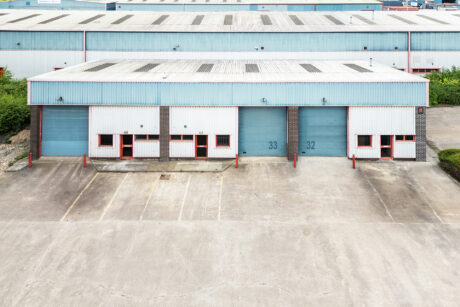 A large industrial warehouse with blue loading bay doors numbered 32 and 33, empty loading area, and no vehicles present.