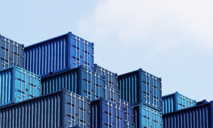 A stack of blue shipping containers is arranged in tiers against a partly cloudy sky.