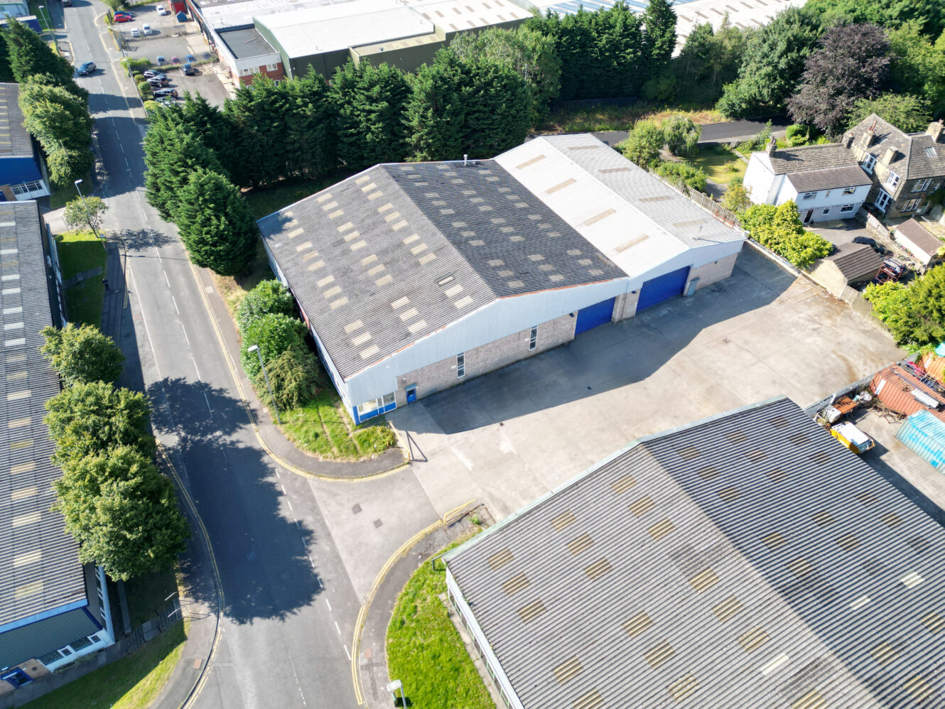 Aerial view of an industrial warehouse with a large parking area, surrounded by roads, trees, and nearby buildings.