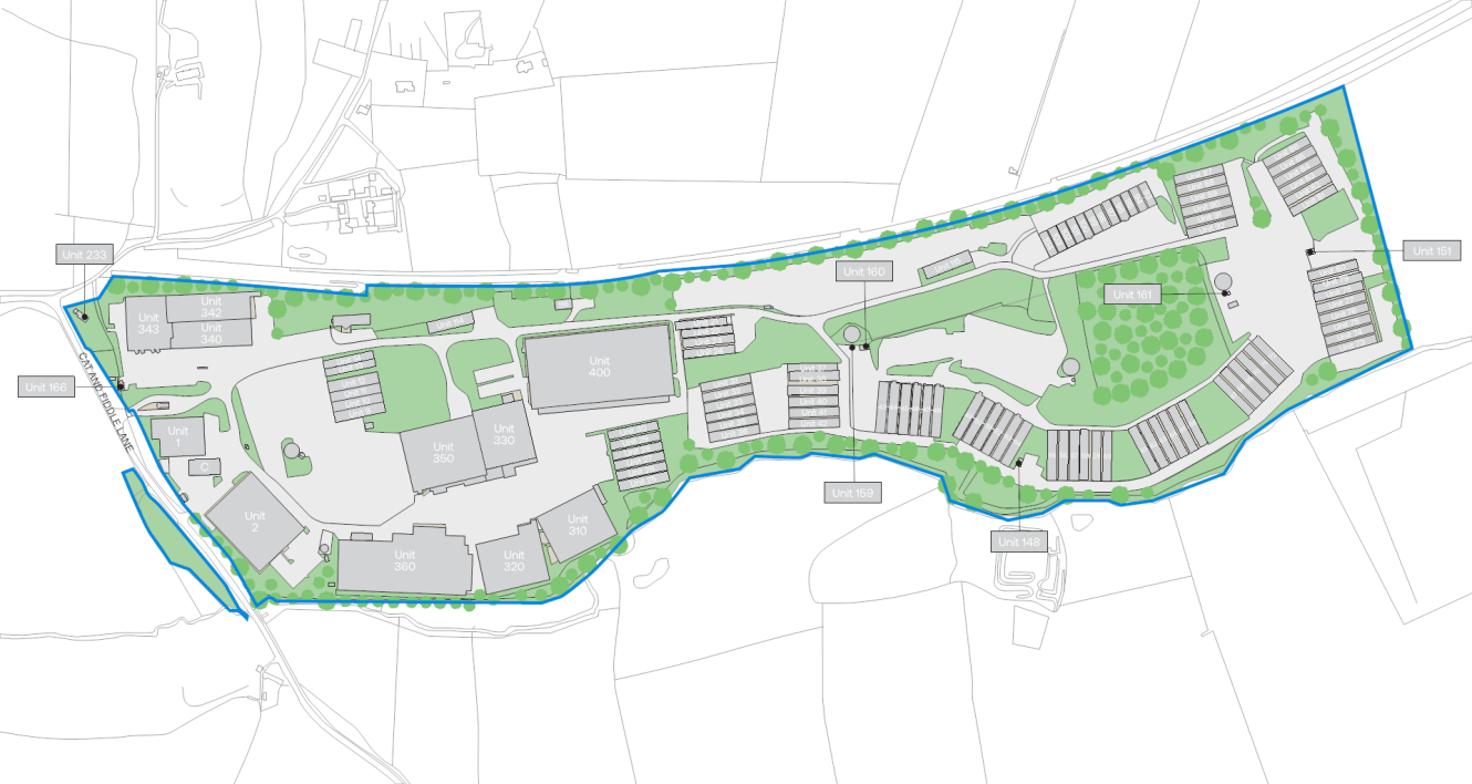 A site plan map showing multiple buildings, parking areas, roads, landscaped green spaces, and labeled plots enclosed by a blue outline boundary.