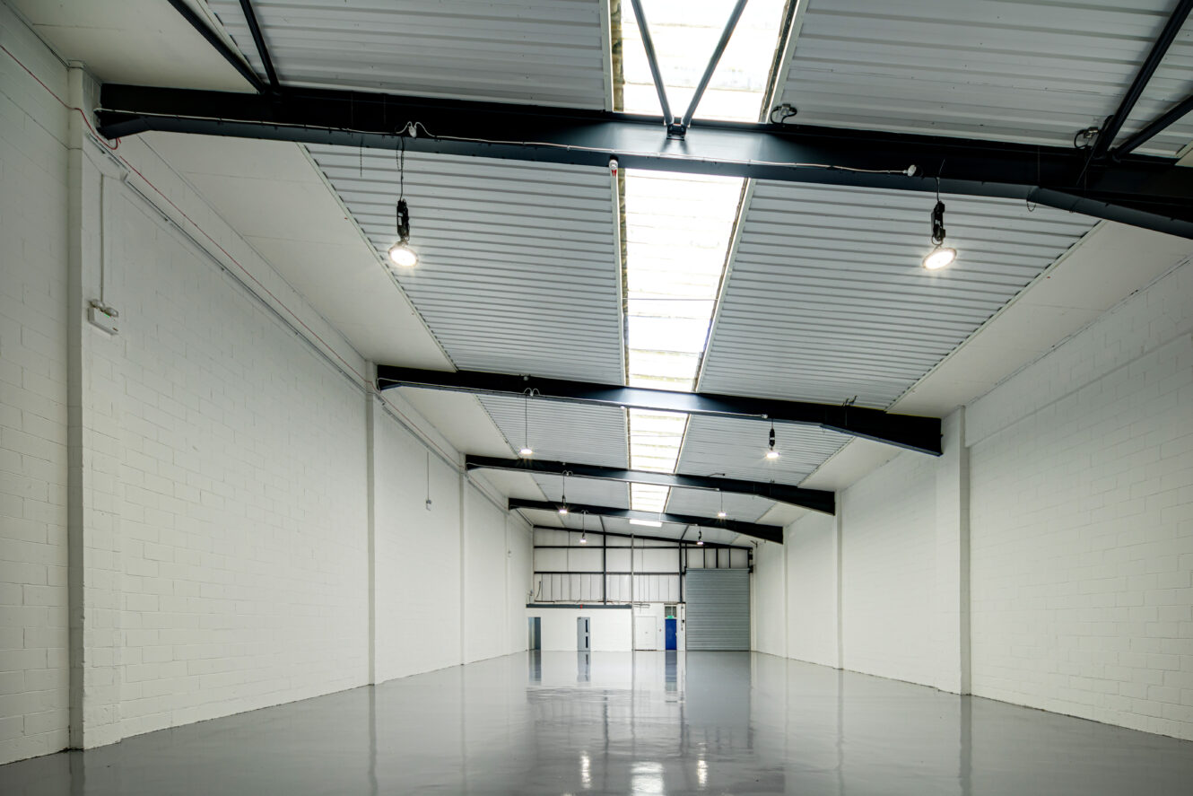 Large empty industrial warehouse with white walls, a polished concrete floor, exposed beams, and skylights letting in natural light.