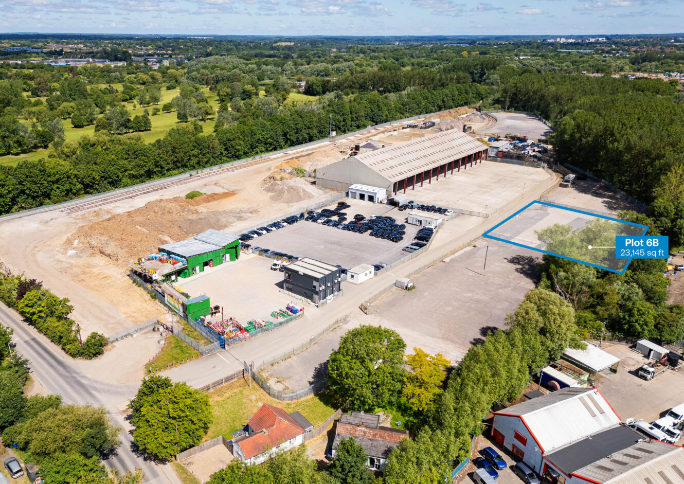 Aerial view of an industrial site with large buildings, parked vehicles, storage areas, and a plot labeled Plot 8B, 23,445 sq ft outlined in blue on the right side.