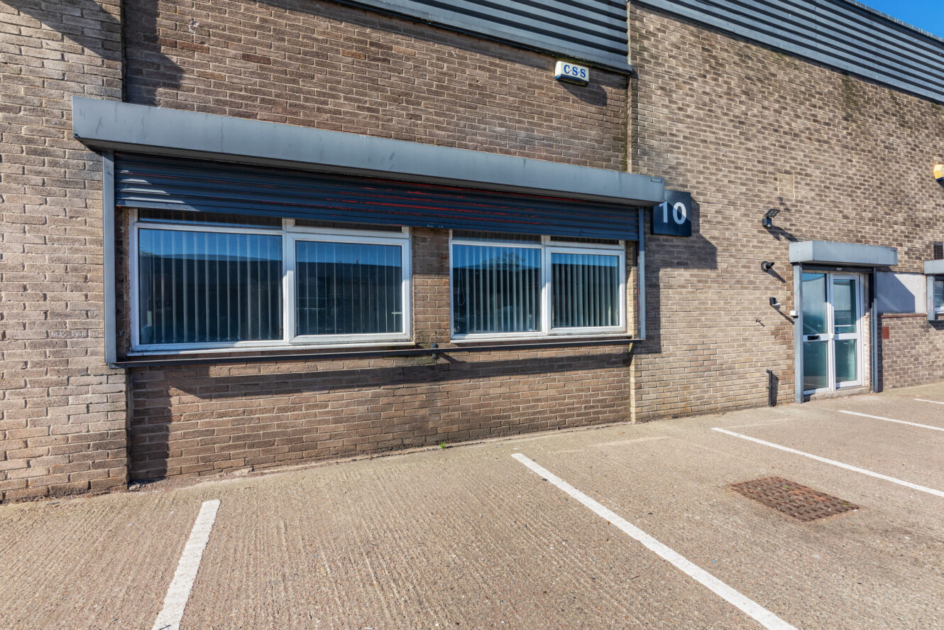 A brick industrial building with large windows, a glass door, and the number 10 displayed, next to empty parking spaces.