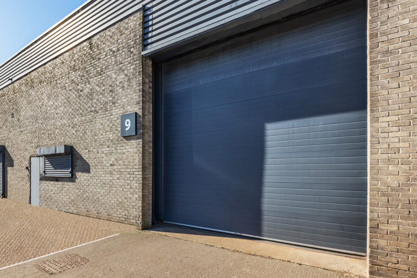 A large gray industrial garage door on a brick building with a number 9 sign and a small window and door to the left.