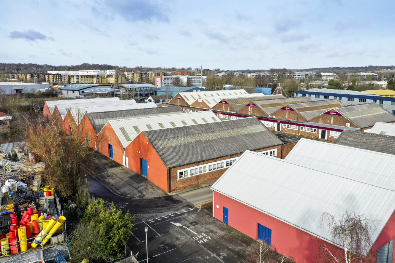 Aerial view of several large industrial warehouse buildings with red brick walls and grey roofs in an industrial estate.