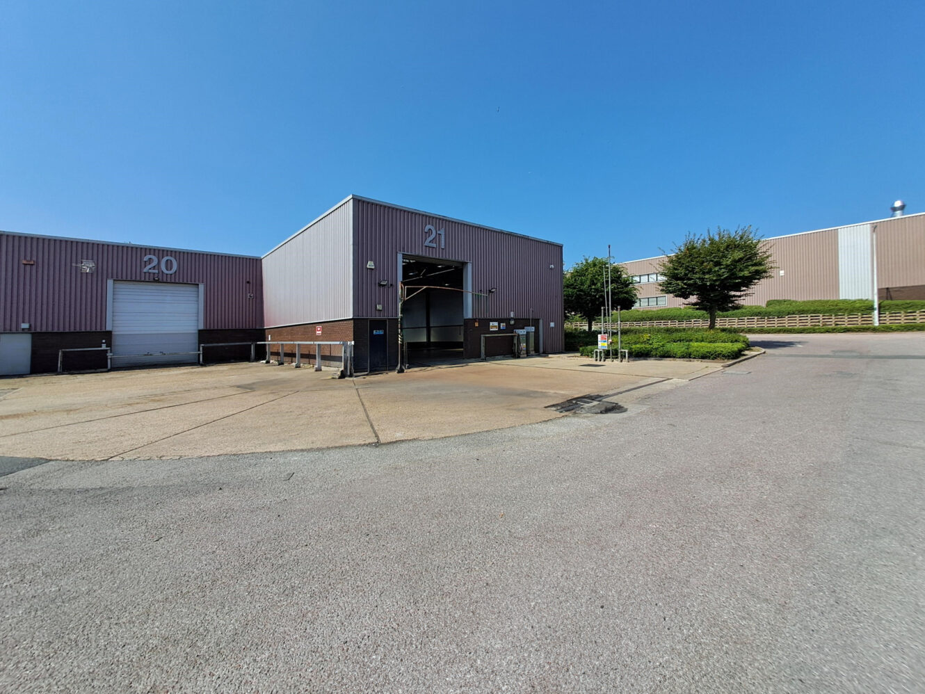 A warehouse loading bay labeled 21 with an open entrance, adjacent to unit 20, under a clear blue sky in an industrial area.