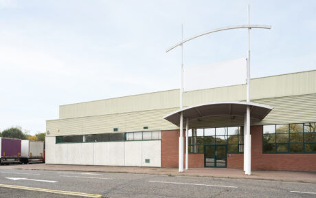 A vacant commercial building with a blank white sign above the entrance, glass doors, and large windows facing a quiet street.